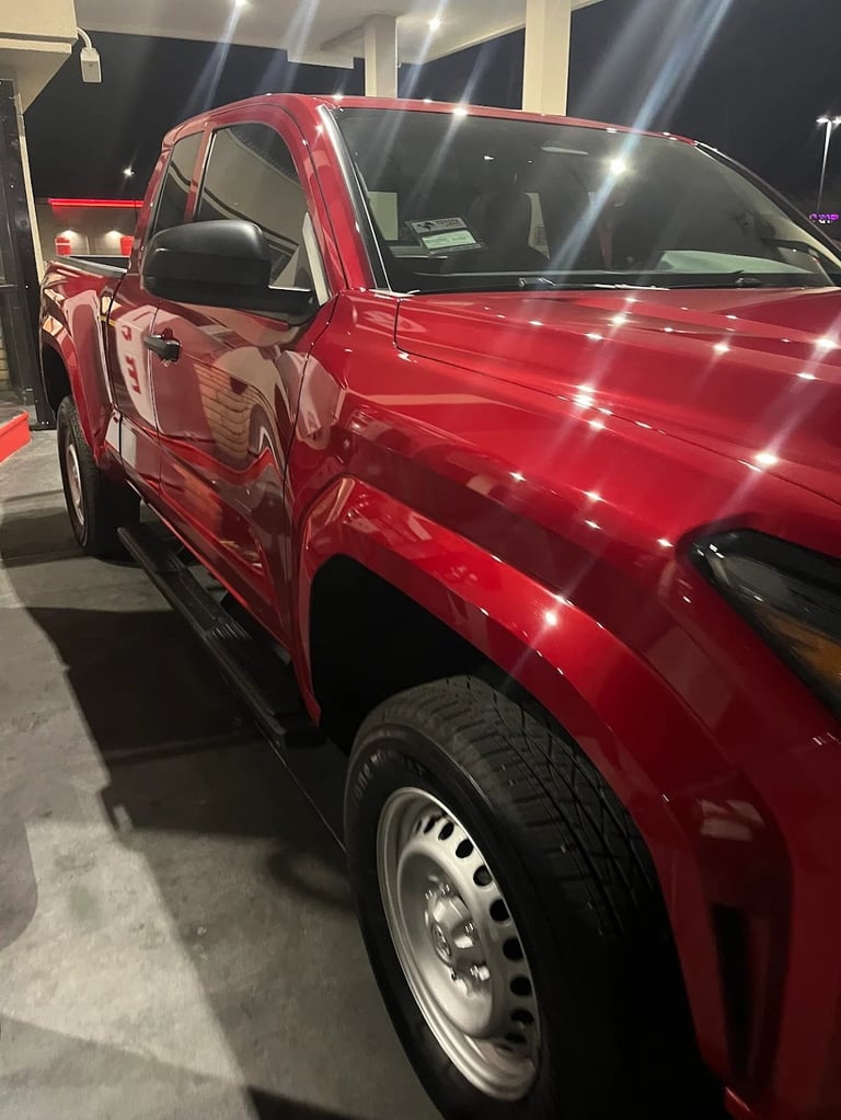 Red pickup truck on display at night with driver side door open, showing black interior and alloy wheels