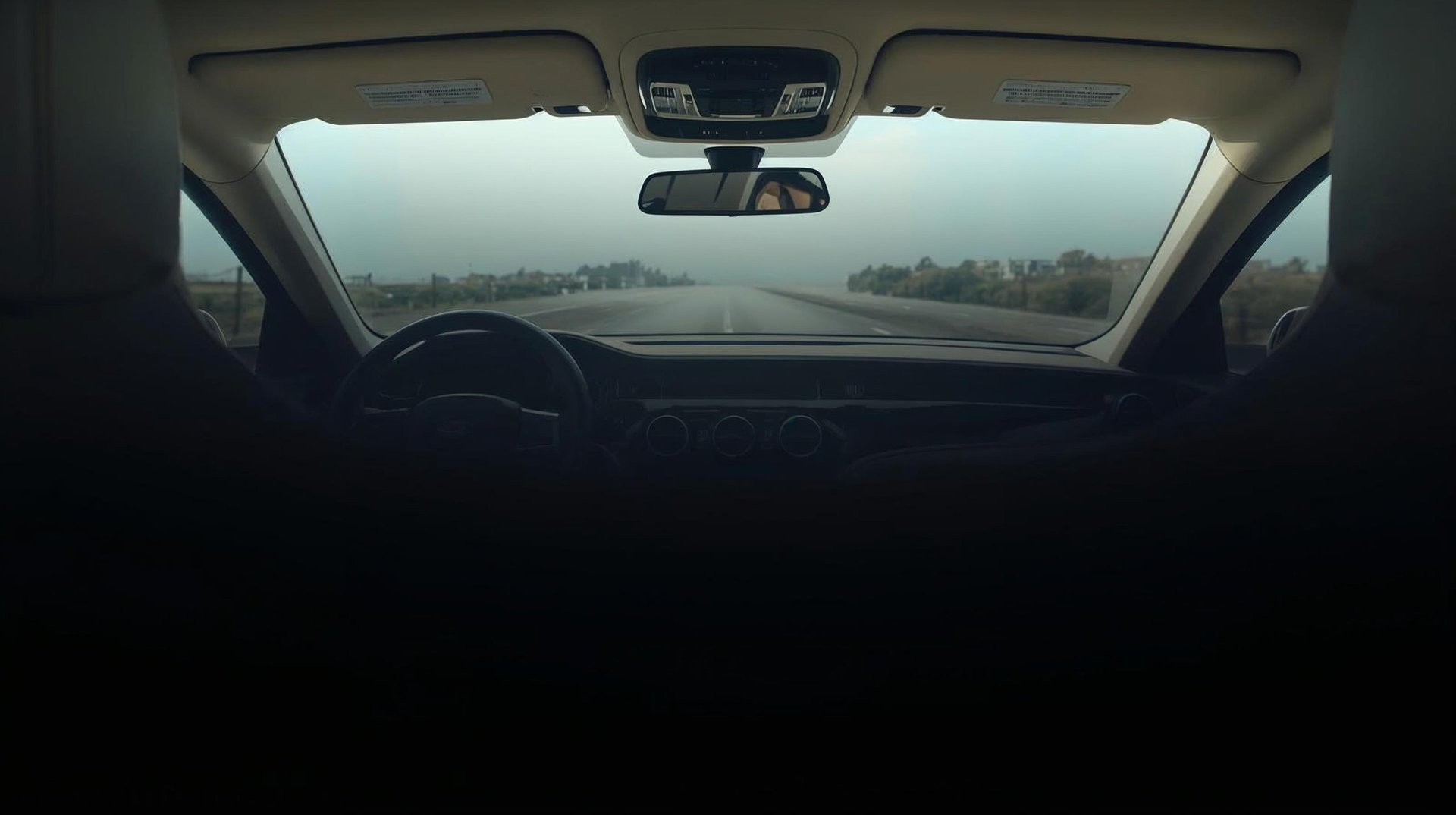 View from inside a car looking out the windshield at a foggy highway with trees in the distance